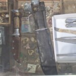 Knives and trinkets displayed in glass case.