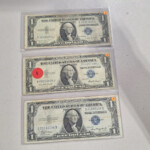 Three US one-dollar bills in plastic sleeves