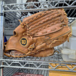 Worn brown Wilson baseball glove on metal shelf