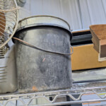 Worn black plastic bucket on metal shelf